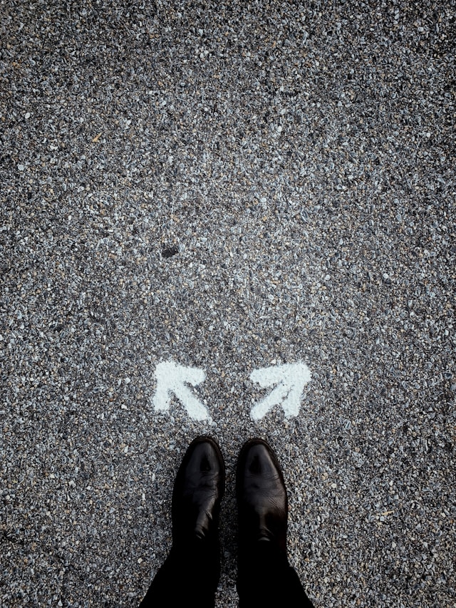 Eine Person mit schwarzen Schuhen steht hinter zwei weißen Pfeilen, die in verschiedene Richtungen zeigen.