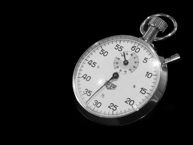 A close-up of a gray stopwatch on a black background.