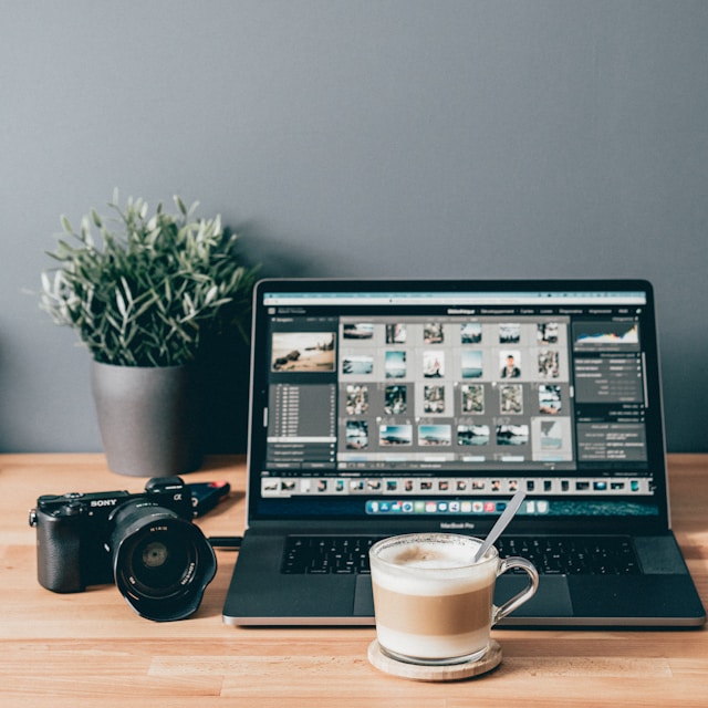 Un MacBook Pro gris con Adobe Lightroom Classic junto a una taza de café y una cámara.