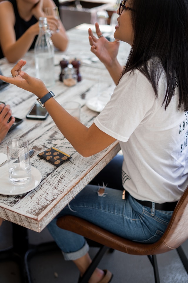 Primer plano de una mujer conversando con otras personas alrededor de una mesa blanca.