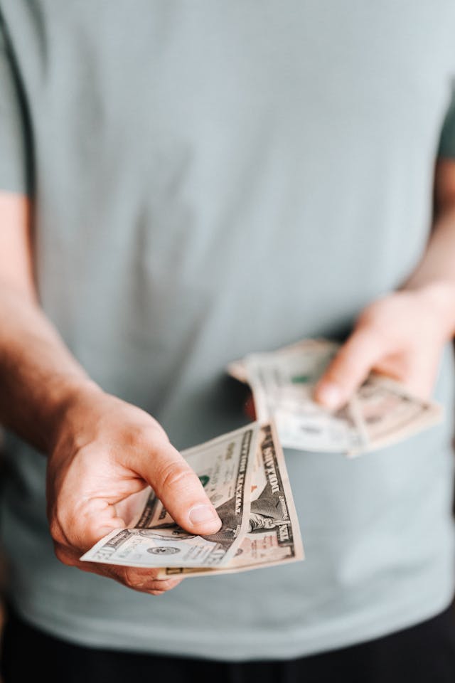 Een persoon met een groen shirt deelt twee bankbiljetten van twintig Amerikaanse dollar uit.