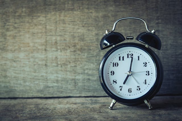 A close-up of a black metallic alarm clock on a brown wooden surface.