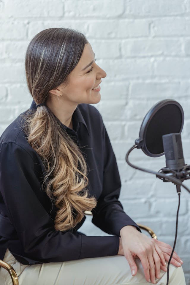 Een vrouw met een zwart shirt zit naast een microfoon met een popfilter.