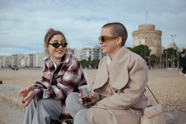 Duas mulheres sentam-se numa parede cinzenta e conversam.