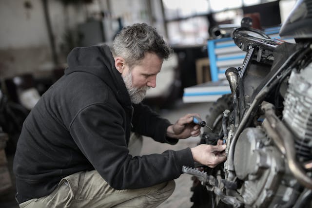 Ein Mann repariert ein schwarzes Motorrad mit einem schwarz-blauen Schraubenzieher. 