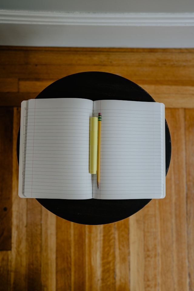 Un cahier avec un surligneur jaune et un crayon jaune sur une table noire.