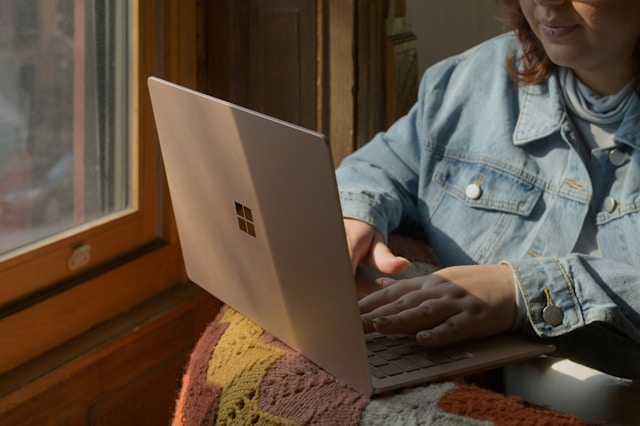 Une femme avec une veste en jean bleue utilise un ordinateur portable Microsoft Surface gris.