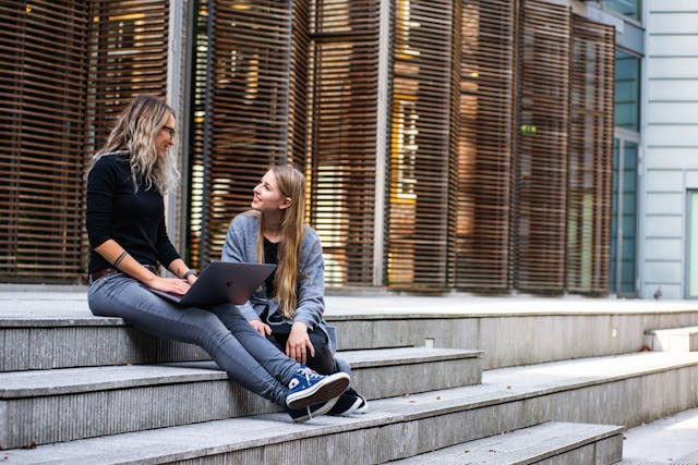 Due donne siedono su una rampa di scale e conversano.