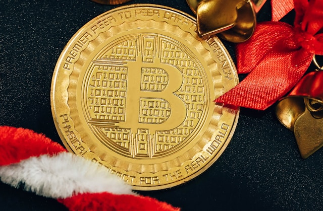 Uma moeda de ouro com o símbolo da Bitcoin rodeada de decorações de Natal vermelhas e brancas.