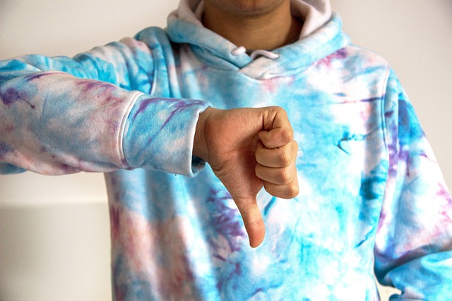 Een persoon met een witte, blauwe en paarse tie-dye hoodie laat duimen omlaag zien.