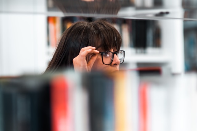 A close-up of a woman with glasses in a library.