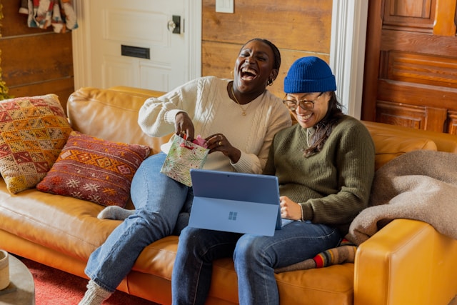 Two women sit on an orange couch and laugh.