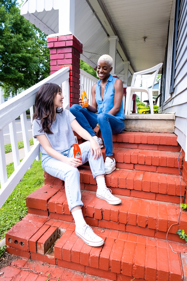 Two women sit on a flight of red stairs and have a conversation.