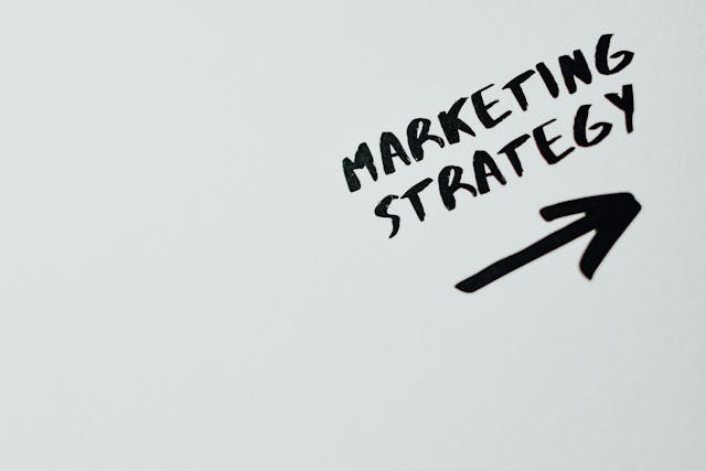 The phrase “marketing strategy” with an arrow on a white surface.