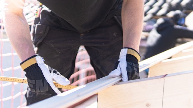 Een persoon met zwart-wit gekleurde handschoenen gebruikt een geel meetlint.