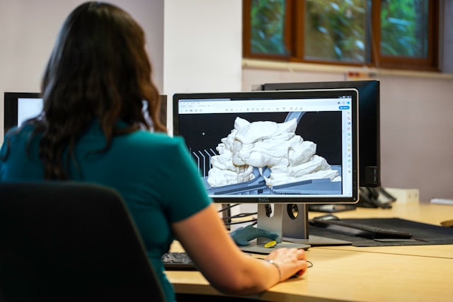 Een vrouw in een groen shirt bekijkt een 3D-model op een Dell monitor.