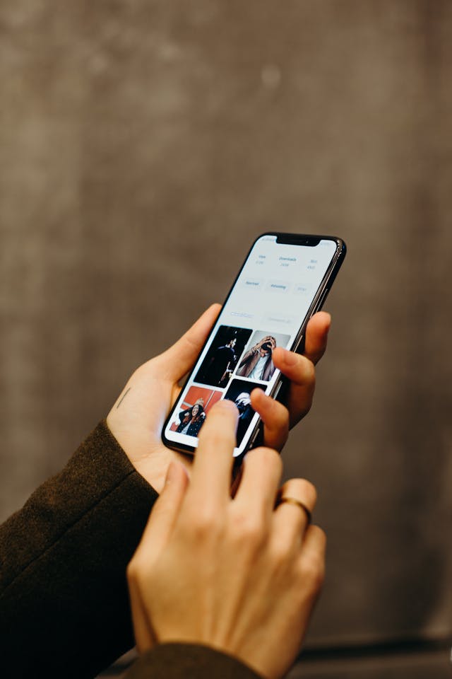 A person with brown sleeves uses a black iPhone to view images.