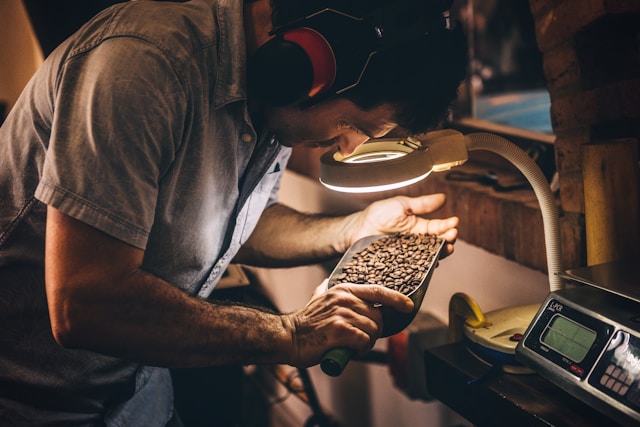 Une personne vêtue d'une chemise bleu clair examine des grains de café à l'aide d'une loupe éclairée.