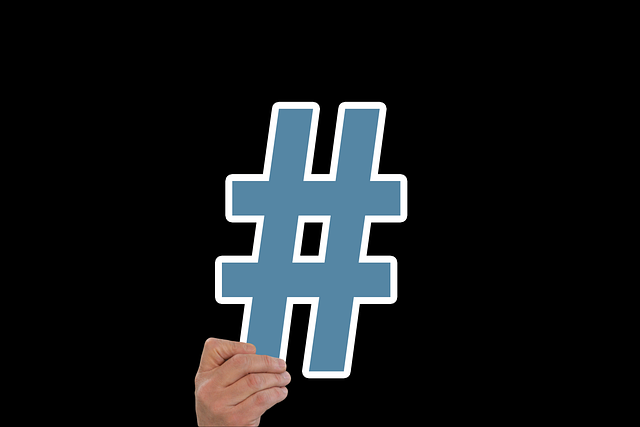 A hand holds a blue hashtag on a black background.