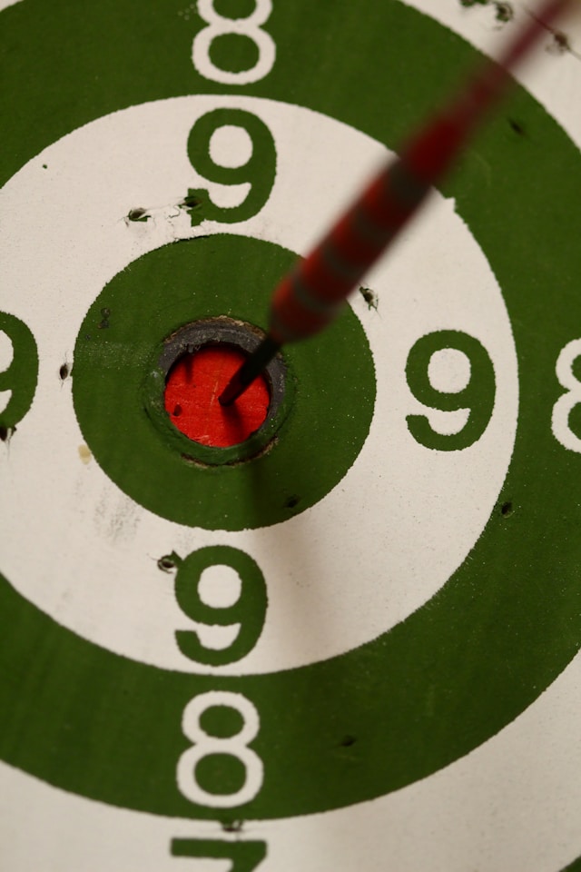 A close-up of a dart in a red bullseye on a white and green dartboard.