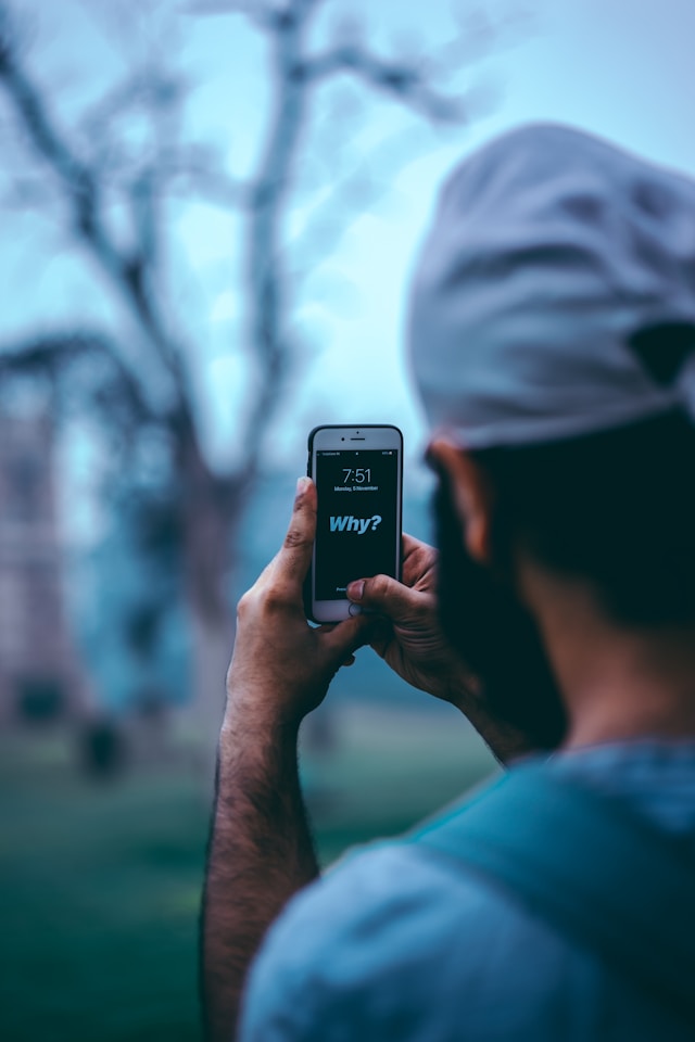 Een man houdt een witte iPhone vast met het woord "Why" op het vergrendelscherm.