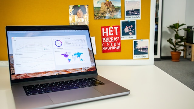 Un MacBook gris avec de nombreux graphiques sur son écran est posé sur un bureau blanc.