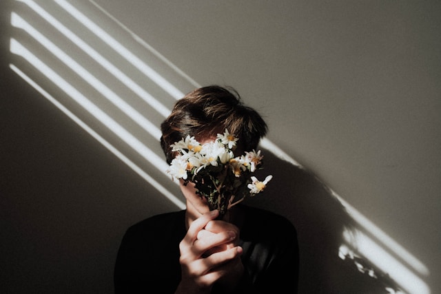 Eine Person mit einem schwarzen Hemd hält sich einen Blumenstrauß vor das Gesicht.