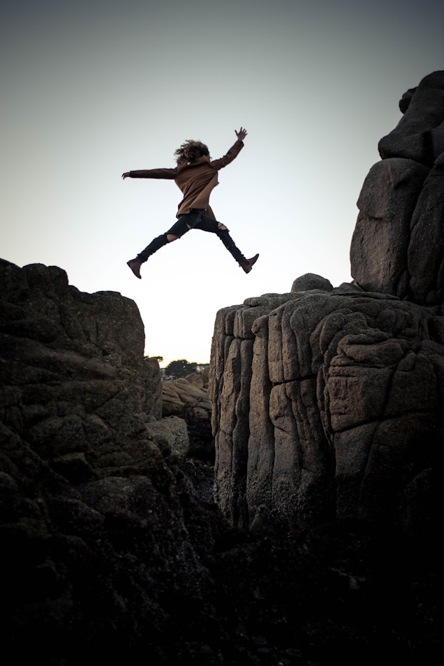 Eine Person mit einem braunen Hemd springt von einem Felsen zum anderen.