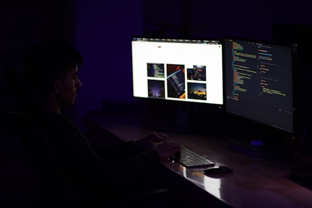 Um homem olha para dois monitores e utiliza o seu teclado.