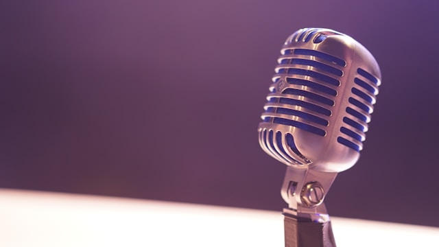 A close-up of a metal microphone on a brown wooden stand.