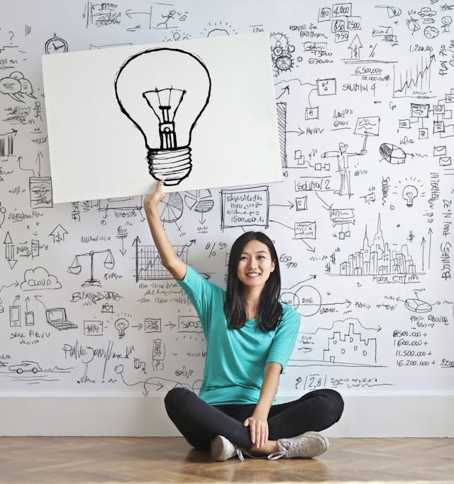 A woman with a cyan shirt holds a light bulb drawing.