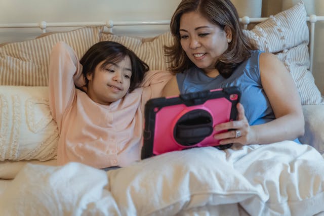 A mother holds a tablet with a pink case and shows it to her child.