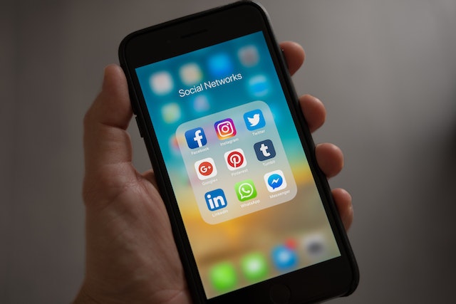 O imagine a unei persoane care ține în mână un iPhone și care afișează mai multe rețele sociale într-un dosar de aplicații.
