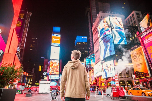 O persoană se uită la mai multe reclame digitale de pe mai multe clădiri din New York.