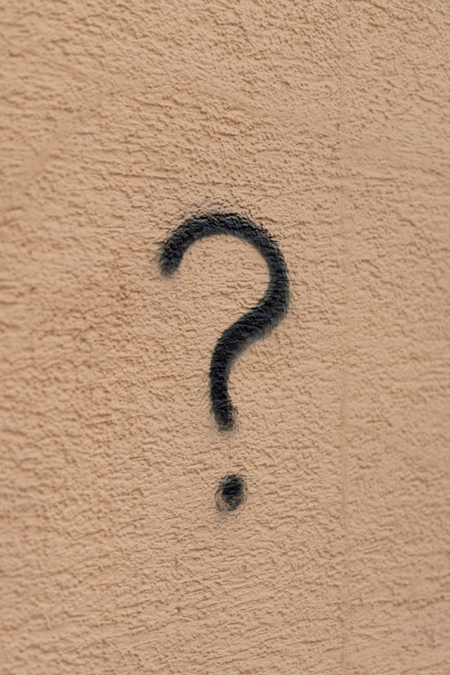 Un semn de întrebare negru pe un perete maro deschis.
