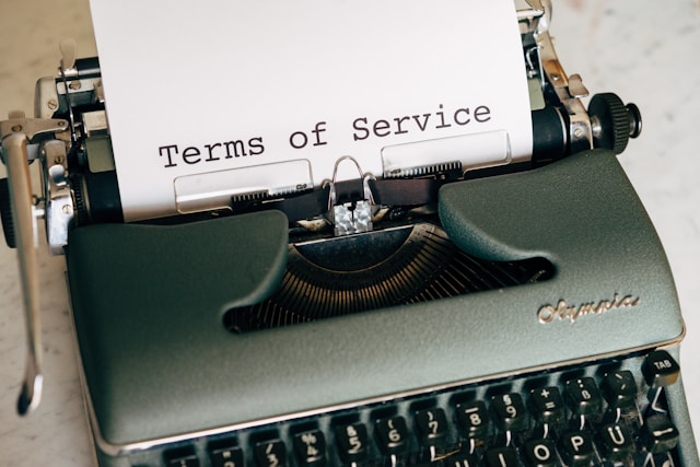 Un prim-plan al unei mașini de scris verzi cu cuvântul "termeni de serviciu" pe o foaie de hârtie albă.
