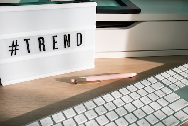 Bir masa üzerinde "#TREND" yazılı bir klavye, kalem ve ışık kutusunun fotoğrafı.
